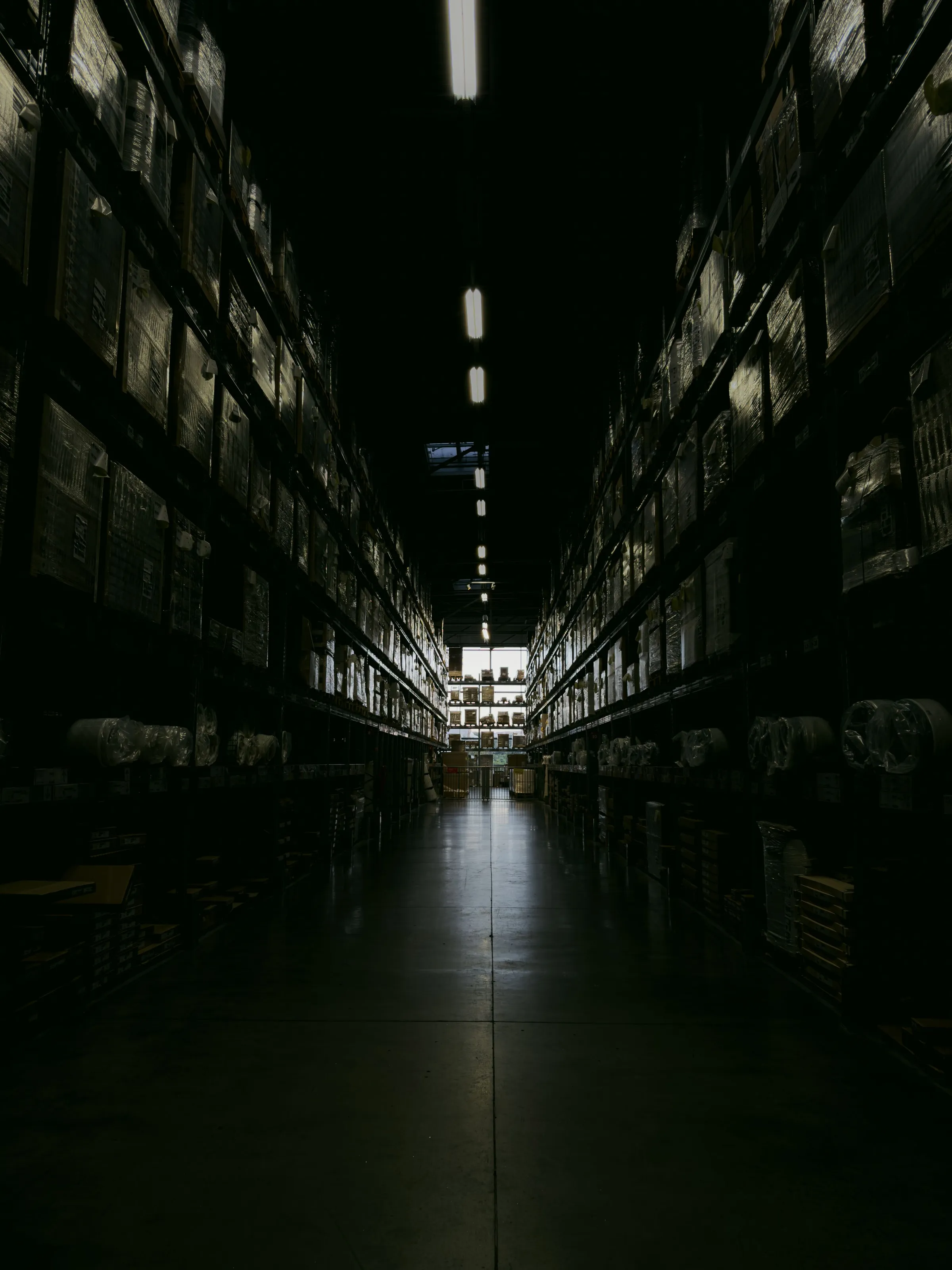 A long, dimly lit warehouse aisle between tall racks